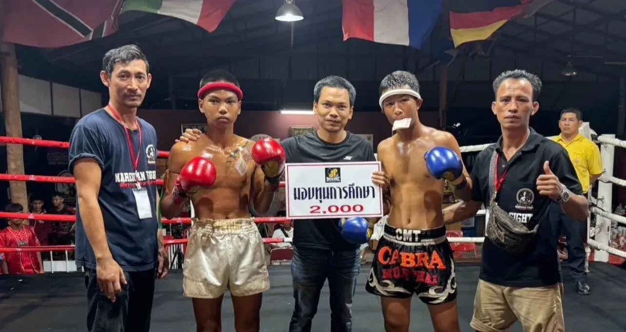 Men and young boys standing in a boxing ring raising a 2000 Baht check